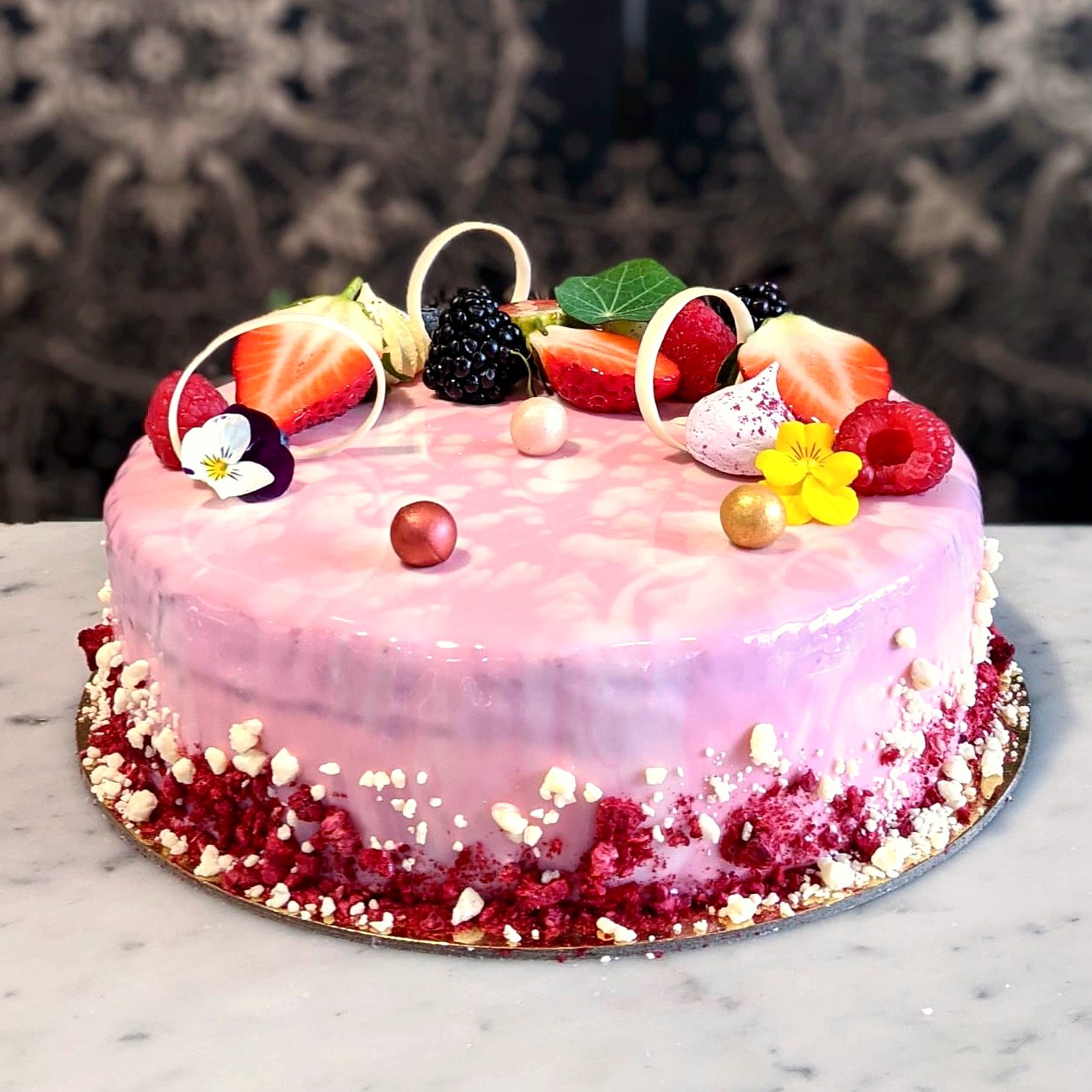 A pink lychee and raspberry mousse cake decorated with fresh berries and edible flowers