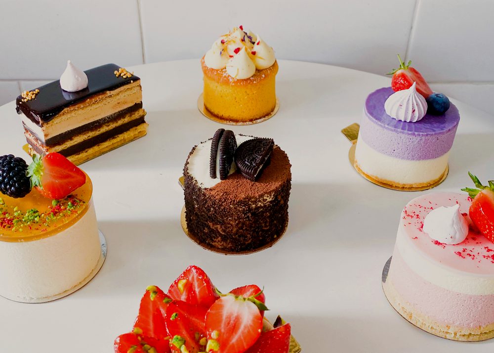 A spread of Strawberry Fields Patisserie's individual mousse cakes and desserts on a marble table