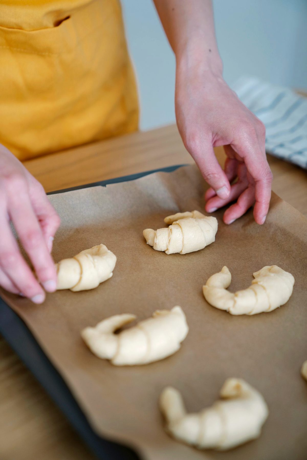 Hands shaping raw croissant dough on a baking tray, ready for the oven